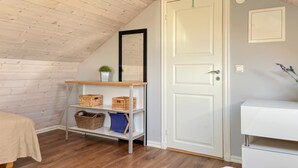 Ein Zimmer mit schrägem Dach, einer weißen Tür, einer kleinen Ablage mit Körben, einem Spiegel und einem weißen Schrank.