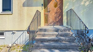 Eine Reihe aus Steinstufen führt zu einer braunen Tür mit Rautenmuster, begleitet von schwarzen Metallgeländern.
