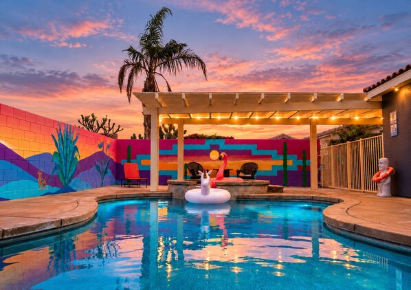 A swimming pool with a colorful mural, a flamingo float, and a palm tree.
