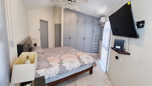 A bedroom with a bed, a ceiling fan, a wardrobe, and a TV mounted on the wall.