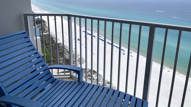 A balcony with a blue chair overlooking a beach with clear turquoise water and white sand.