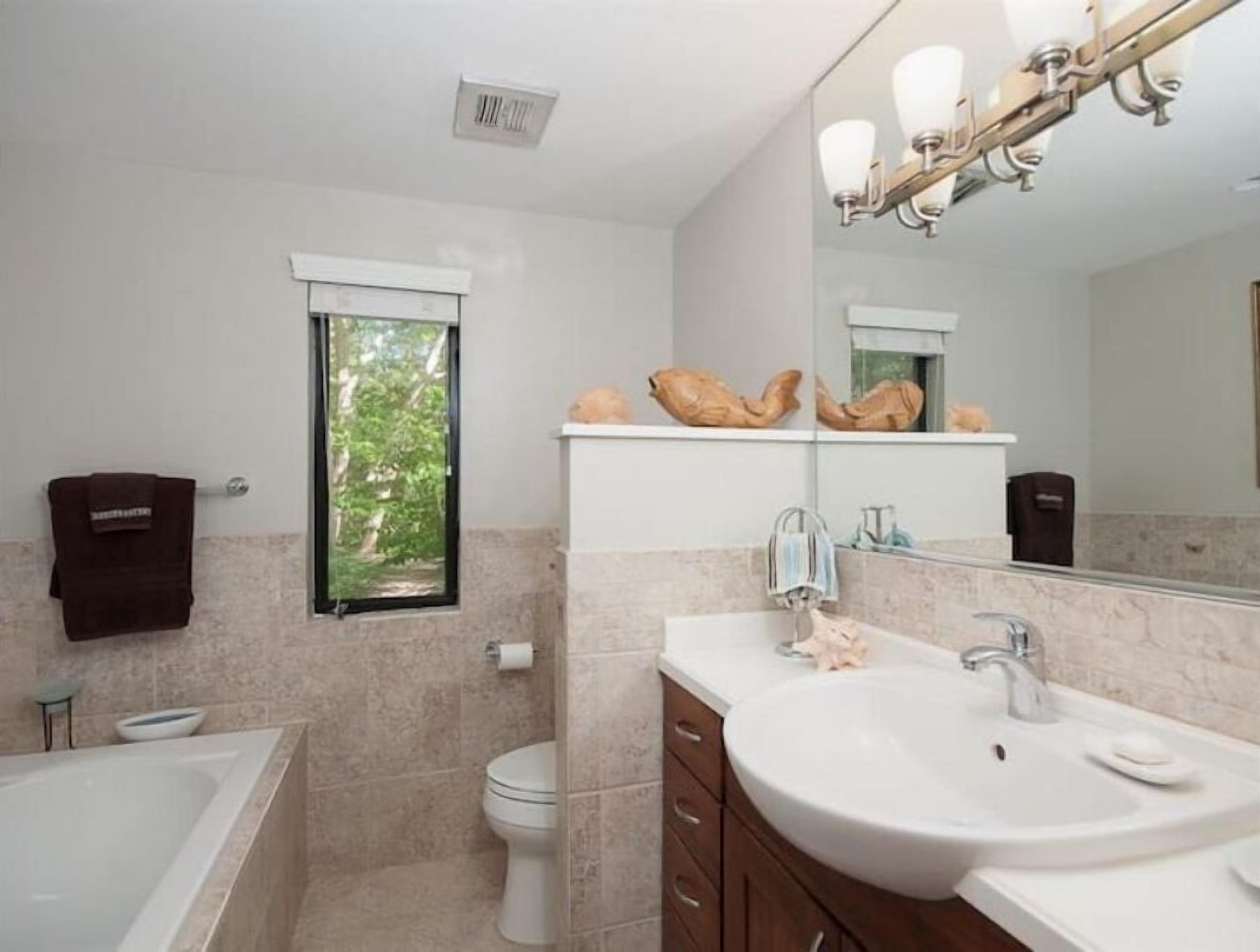 Une salle de bain moderne avec une baignoire, un lavabo et des toilettes. Il y a une fenêtre donnant sur des arbres, ainsi qu'un porte-serviettes sur lequel est accrochée une serviette.