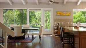 Una cocina moderna con ventanas amplias, un comedor con mesa y sillas, y una escalera de madera.