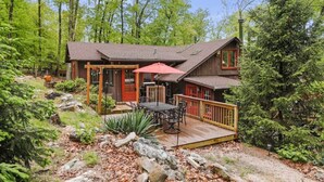 A cabin with a deck, outdoor seating, and a red umbrella.