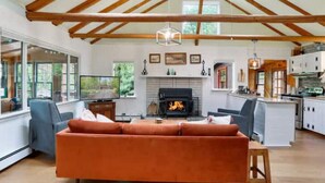 A spacious living room with a fireplace, a sofa, and a dining area with a kitchen in the background.