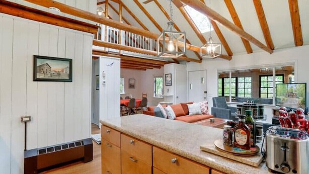 A spacious kitchen with wooden beams, a large island with a toaster, and a dining area with a red table and orange sofa.