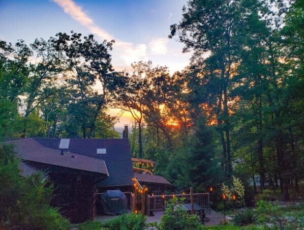 A rustic cabin with a deck and outdoor seating, surrounded by dense forest.