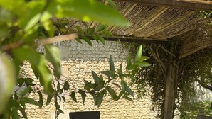 Un patio exterior con pared de piedra, mobiliario de madera y una parrilla.