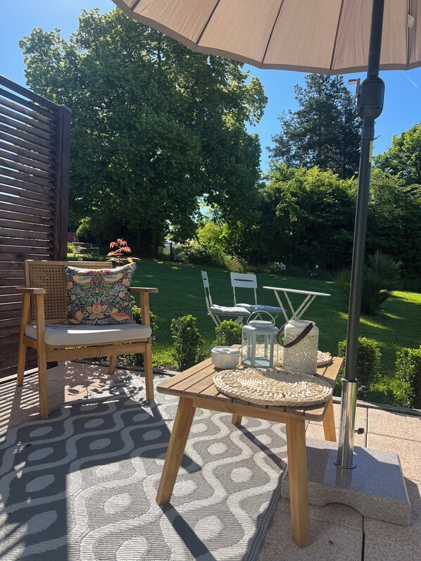 An outdoor patio with a wooden table and chairs, a patterned rug, and a large umbrella. - La Colline de Tilleul - beautiful cottage near Aubeterre with pool 4 Star Rated! (Saint-Romain)