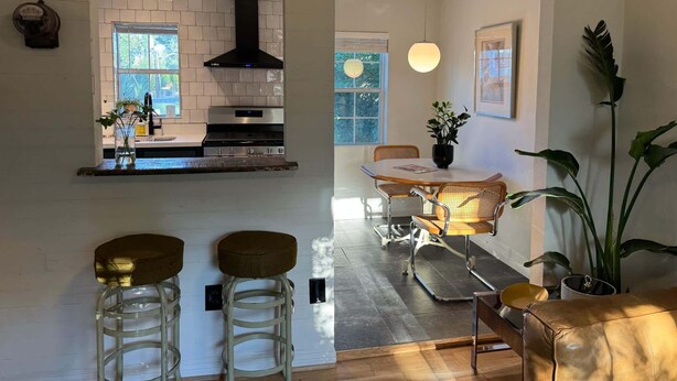 A modern kitchen with white tiles, a black range hood, and a dining area with a wooden table and chairs. - spicewood: w/pool, hot tub, relaxing courtyard (Houston)