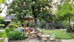 A patio area with a wooden table and chairs, surrounded by a garden and a small lawn. - spicewood: w/pool, hot tub, relaxing courtyard (Houston)
