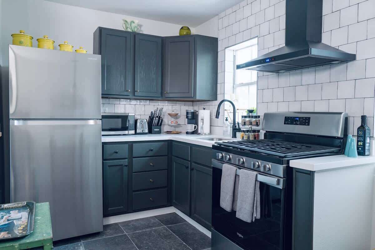 A modern kitchen with dark cabinets, a stainless steel refrigerator, a stove, and a microwave.