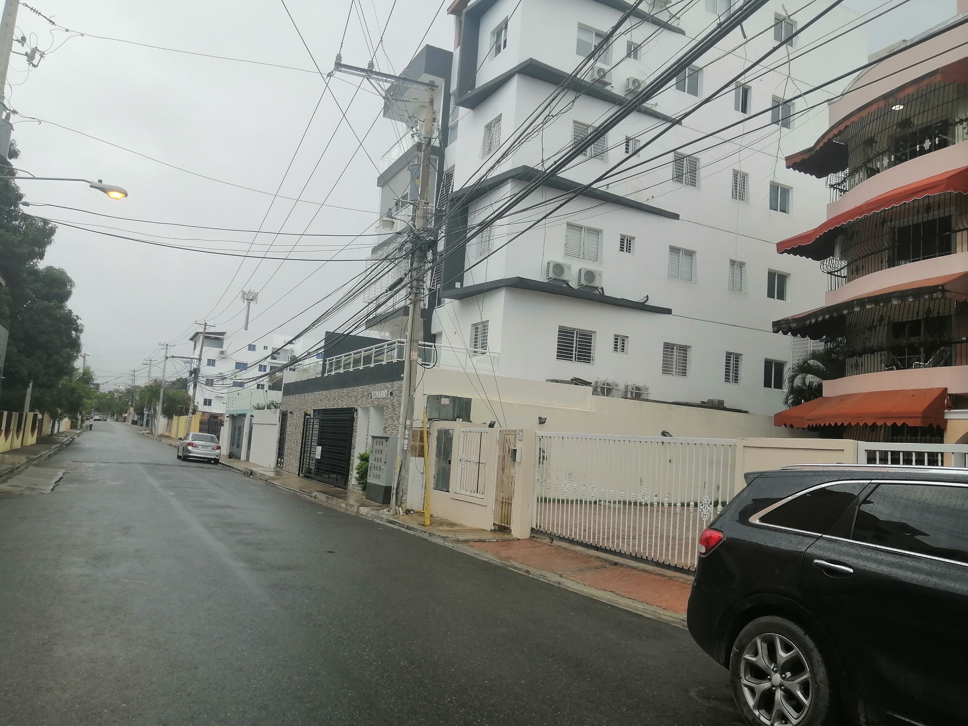 Uma rua com edifícios, um carro e uma cerca.