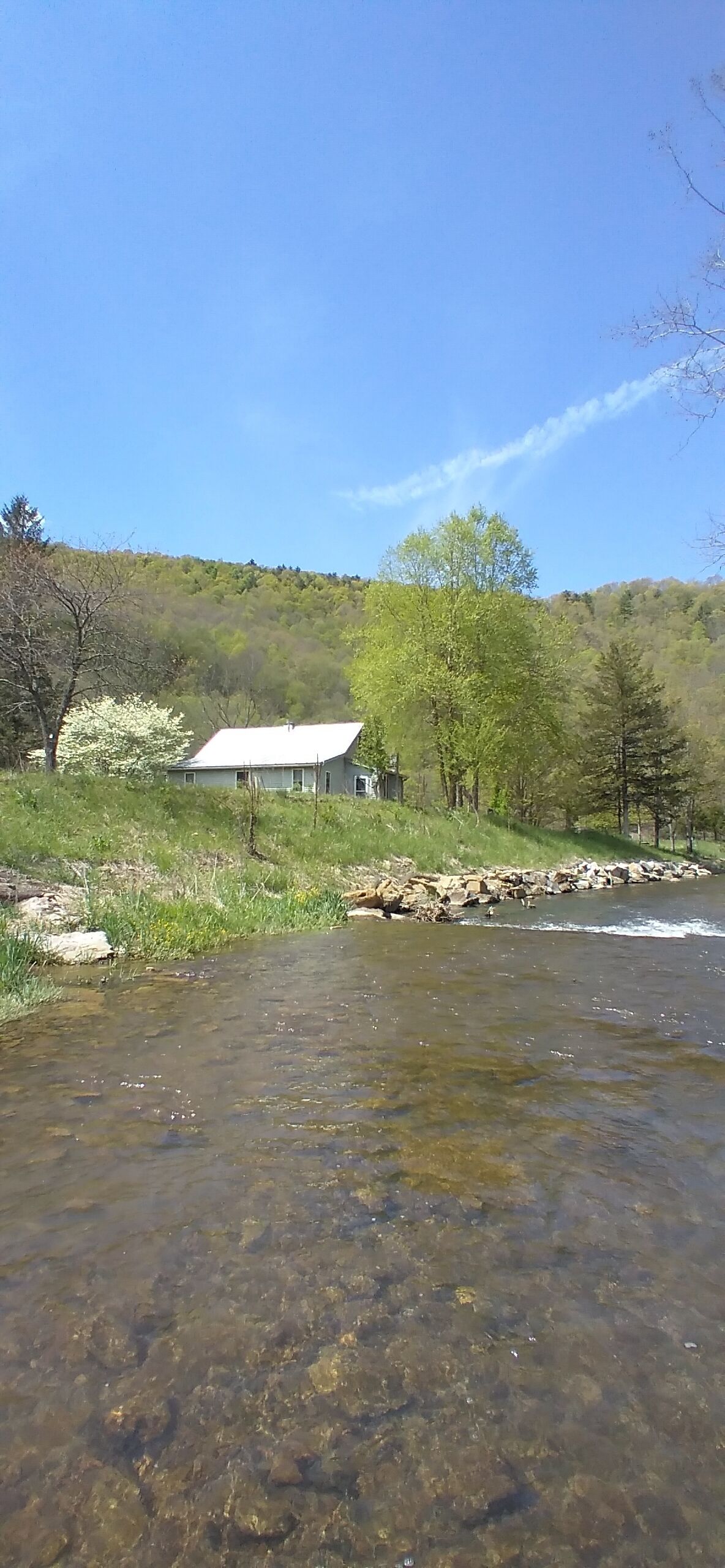 A clear stream with a house in the background.