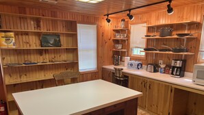 Une cuisine de style rustique, avec des éléments en bois, un îlot central, des étagères en bois et une fen être équipée de stores.