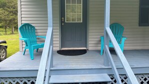 Un porche avec deux chaises turquoise, une porte grise et un paillasson noir.