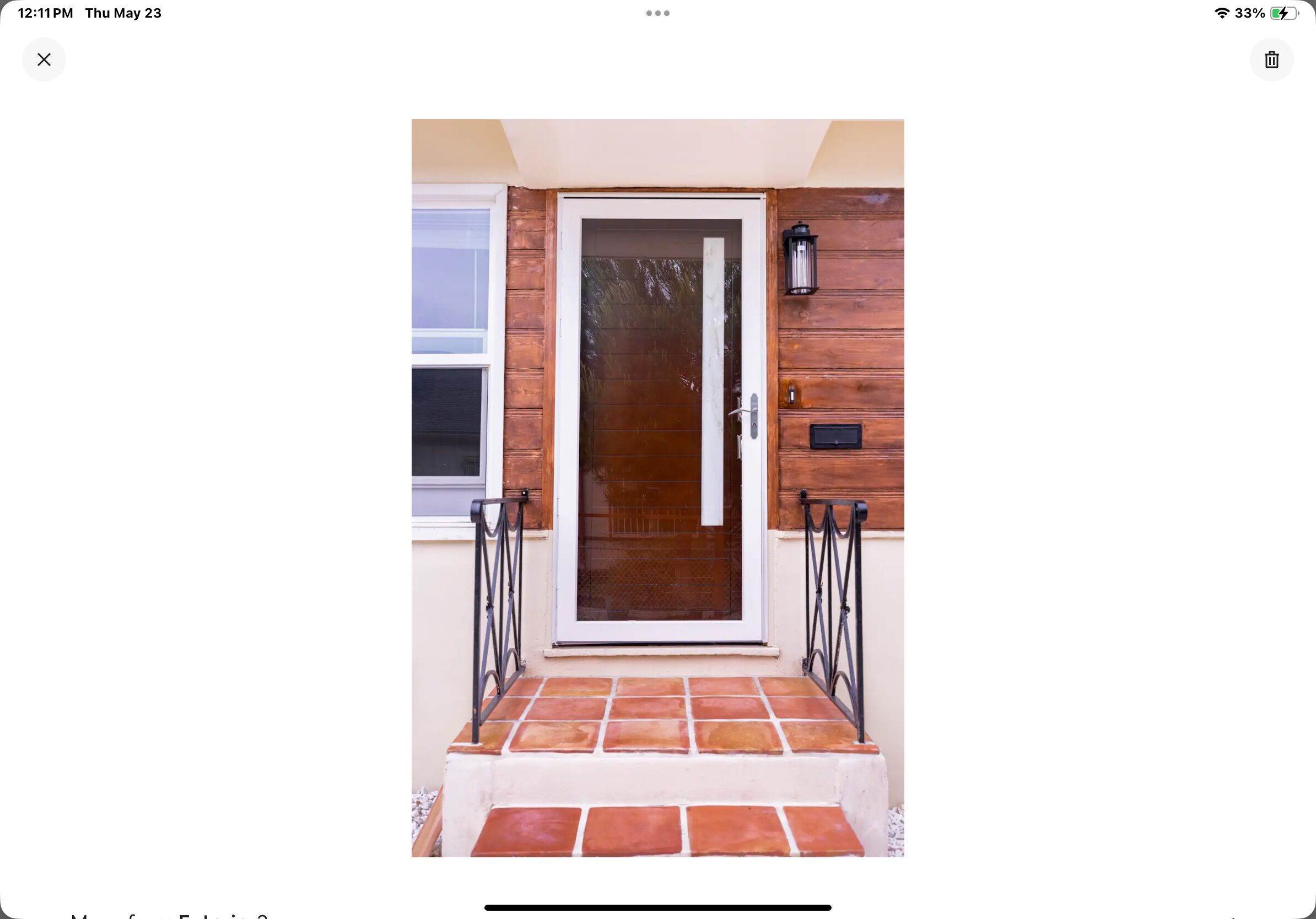 Une porte en bois avec un panneau de verre, encadrée de barreaux métalliques, qui donne sur un hall d’entrée carrelé.