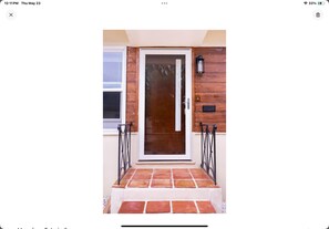 Une porte en bois avec un panneau de verre, encadrée de barreaux métalliques, qui donne sur un hall d’entrée carrelé.