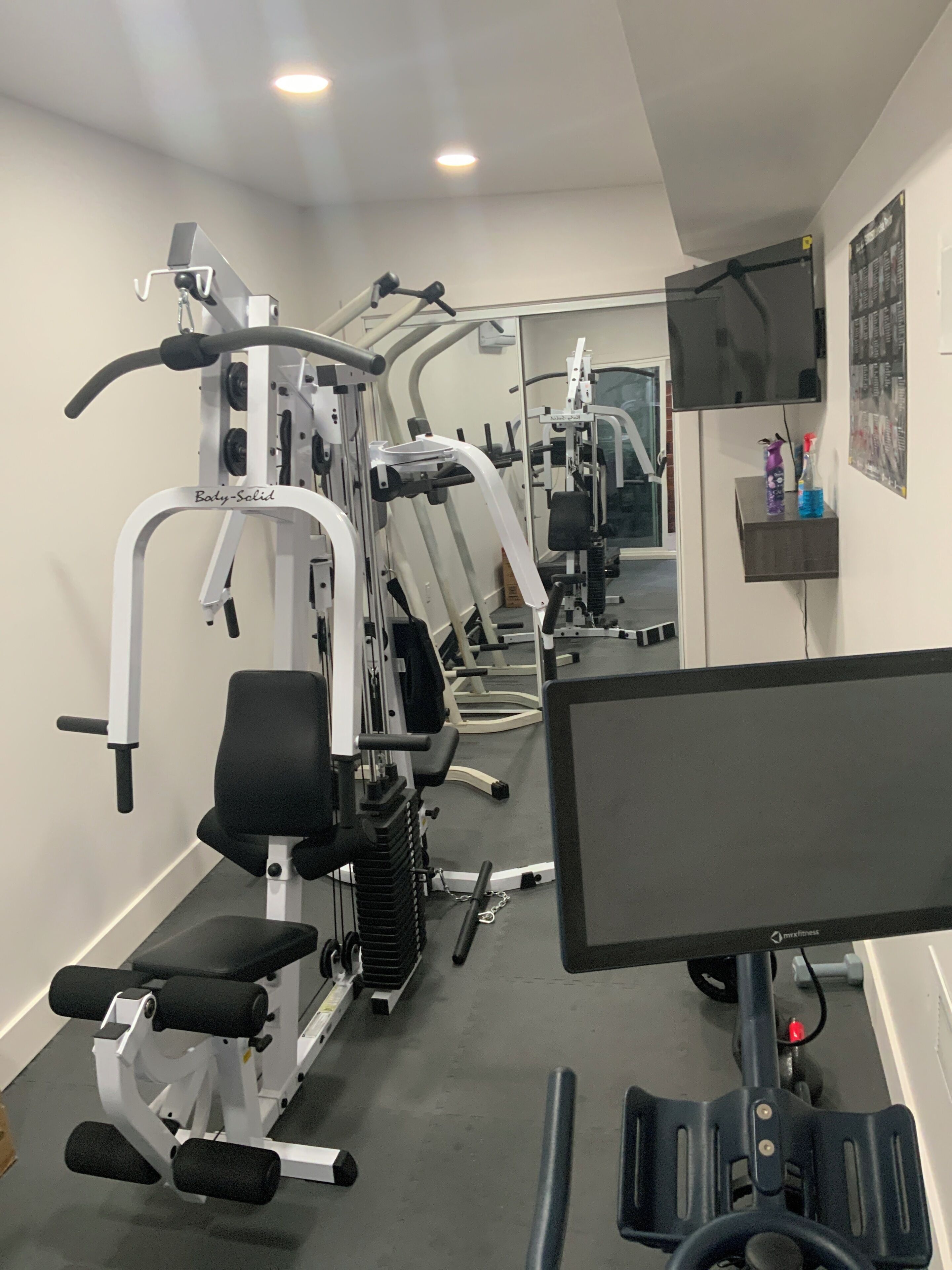 A gym with exercise equipment, a mirror, a TV, and a shelf with bottles.