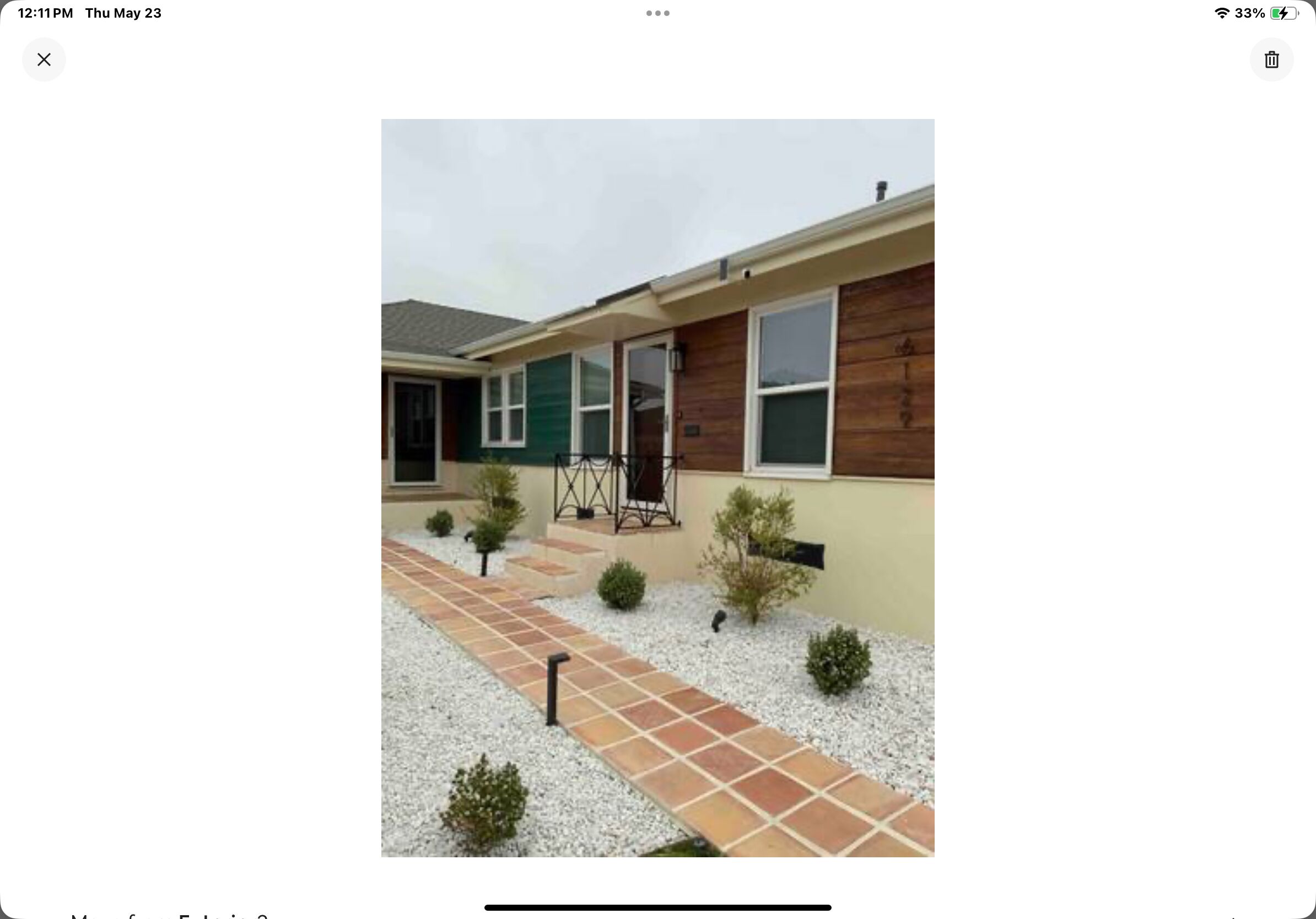Uma casa de dois andares com varanda frontal, um pequeno jardim e um caminho de ladrilhos.