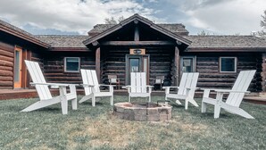 Una cabaña de troncos con un porche delantero, un letrero que dice "Walt Disney" y cuatro sillas Adirondack dispuestas alrededor de un brasero.