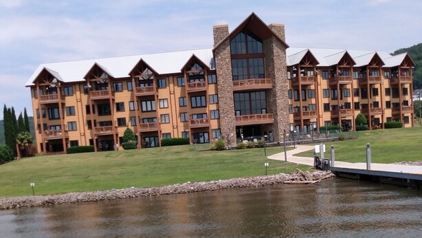 A multi-story hotel with a stone facade and large windows, situated next to a body of water. - Lakeside Condo ~ Close to Everything ~ First Floor ~ Pool ~ Dock ~ Views (Guntersville)