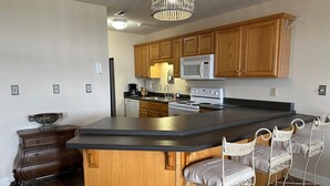 A kitchen with wooden cabinets, a stainless steel refrigerator, a microwave, a stove, and a large island with bar stools. - Lakeside Condo ~ Close to Everything ~ First Floor ~ Pool ~ Dock ~ Views (Guntersville)