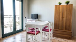 Une pièce avec une table et des chaises blanches, un téléviseur posé sur un meuble et une armoire en bois.