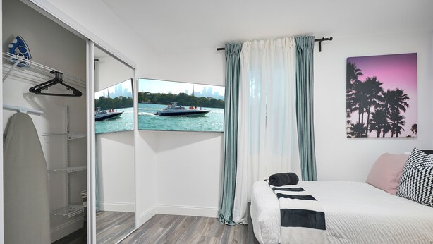 A bedroom with a bed, a closet with a mirror, a view of a boat on water, and a sunset painting. - 4 to 14 Guests 2 Kitchens Deco Retreat BBQ Patio (Miami)