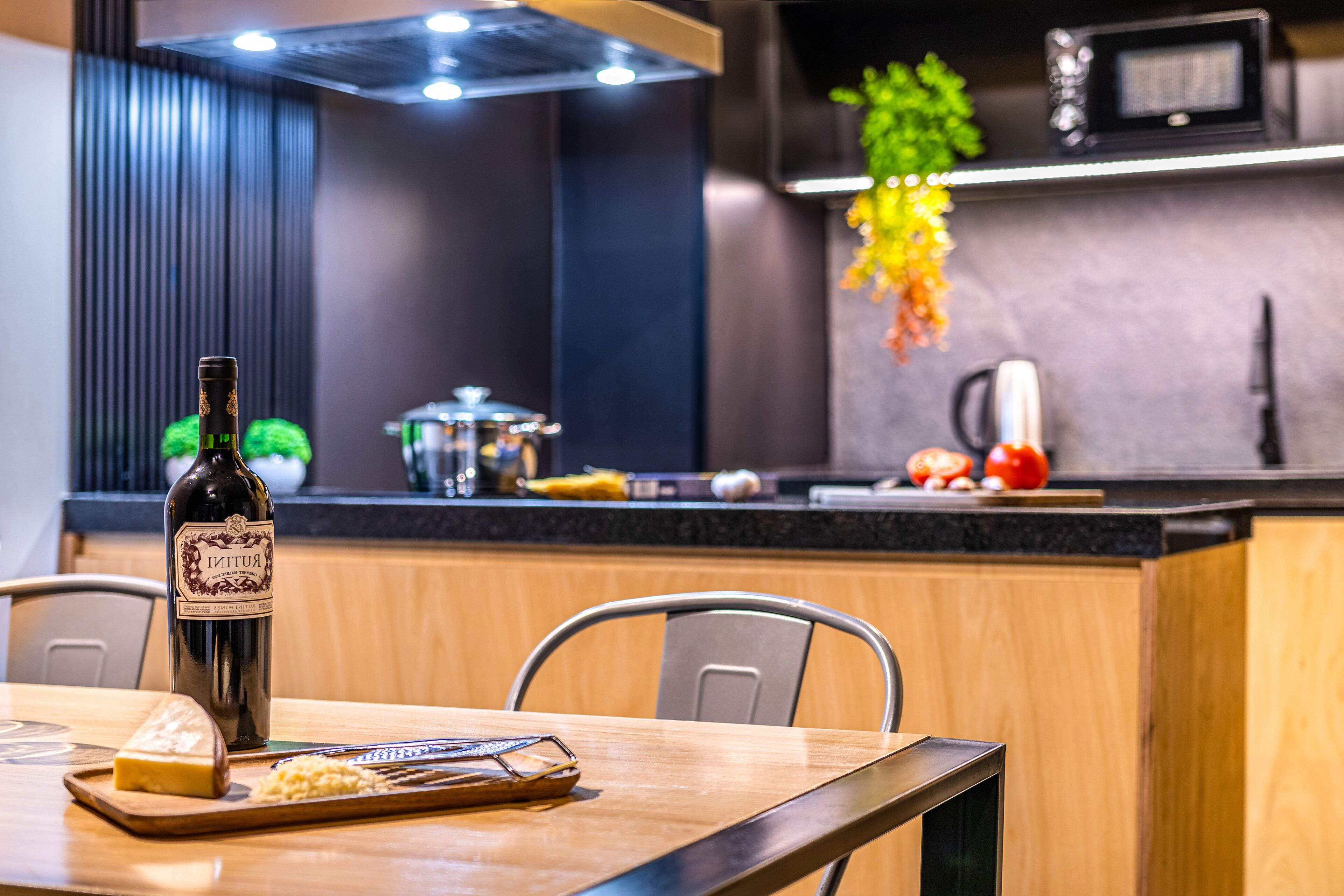 A modern kitchen with a wooden dining table, a bottle of wine, and a cheese board.