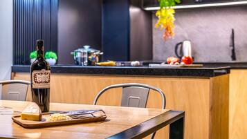 A modern kitchen with a wooden dining table, a bottle of wine, and a cheese board.