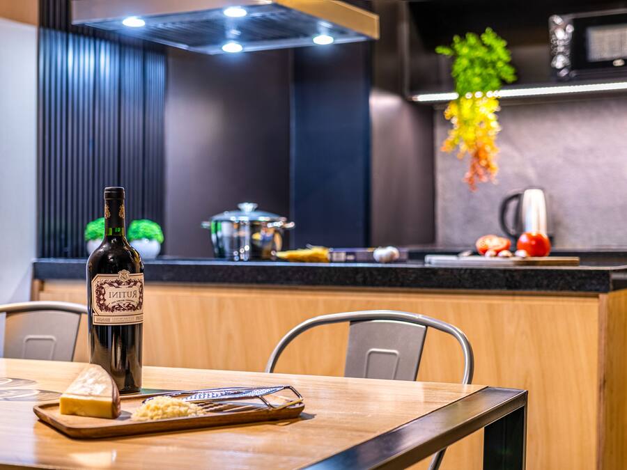 A modern kitchen with a wooden dining table, a bottle of wine, and a cheese board.