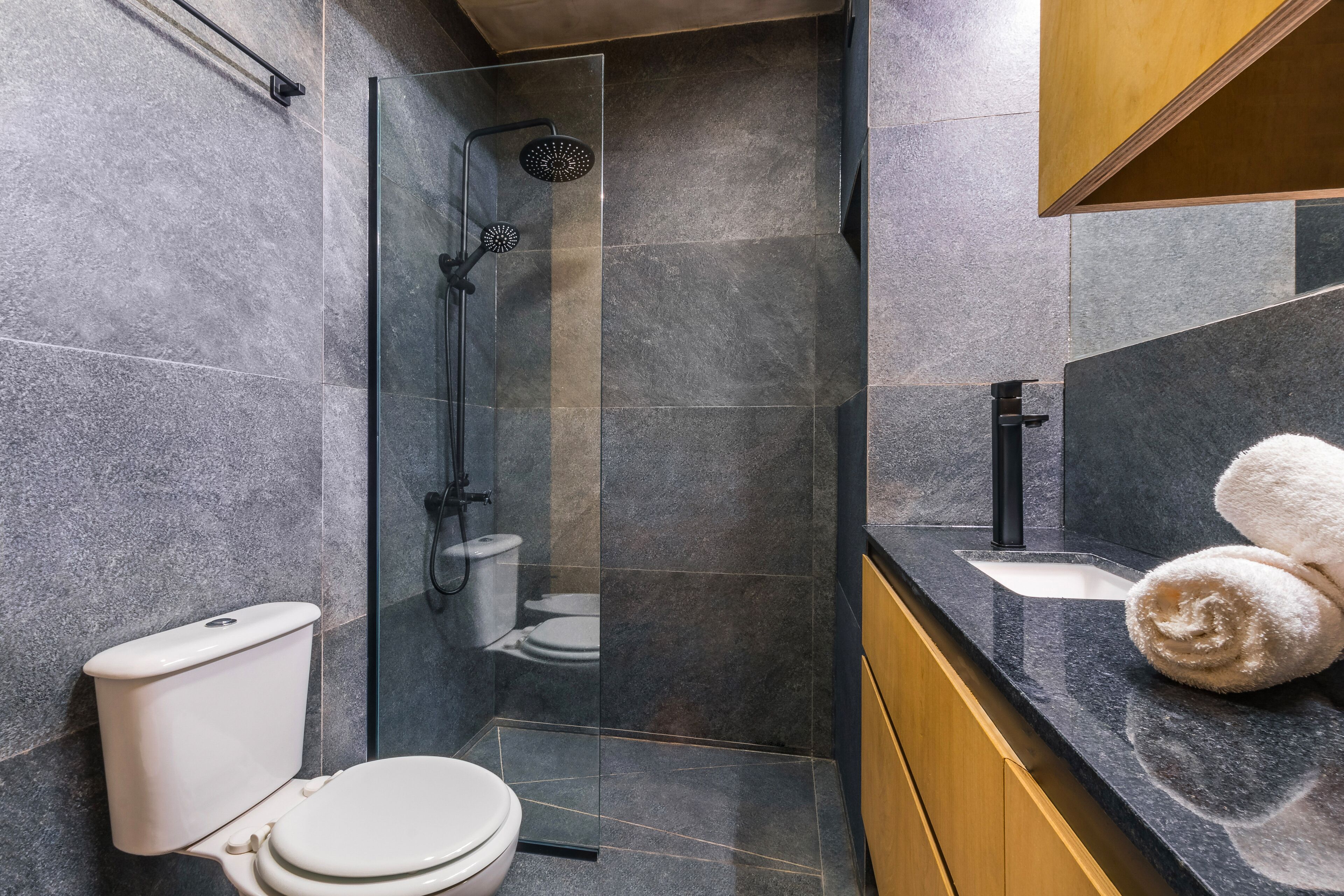 A modern bathroom with a glass-enclosed shower, a white toilet, and a sink with a towel on the counter.