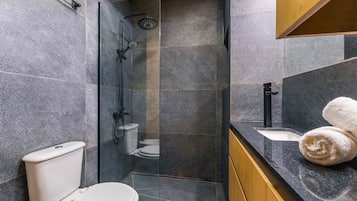 A modern bathroom with a glass-enclosed shower, a white toilet, and a sink with a towel on the counter.