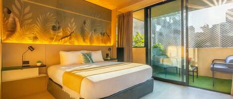 A modern bedroom with a large bed, a nightstand, a desk, and a view of the outdoors through a sliding glass door.