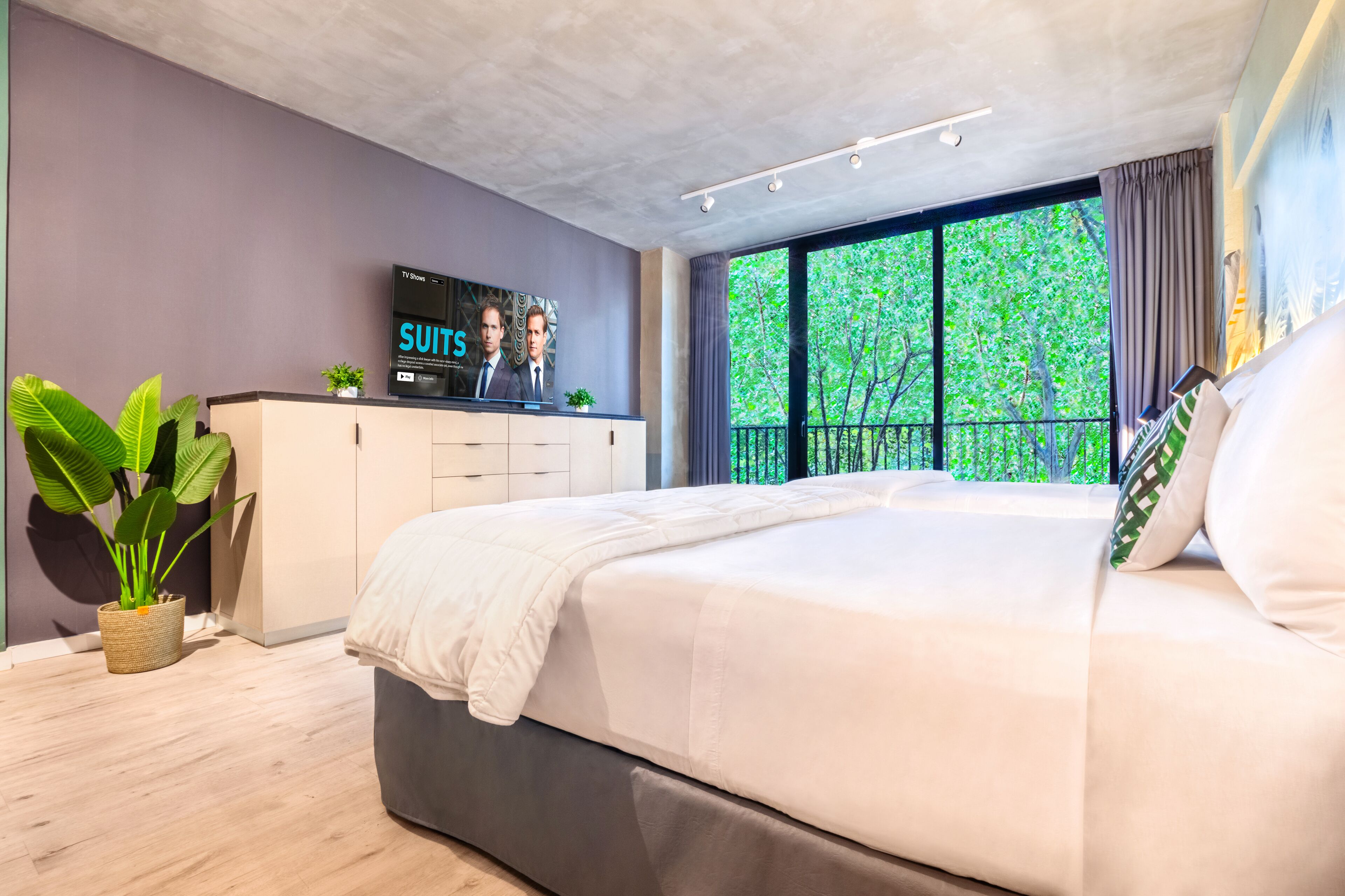 Un dormitorio moderno con una cama grande, un televisor en la pared y vistas a zonas verdes.