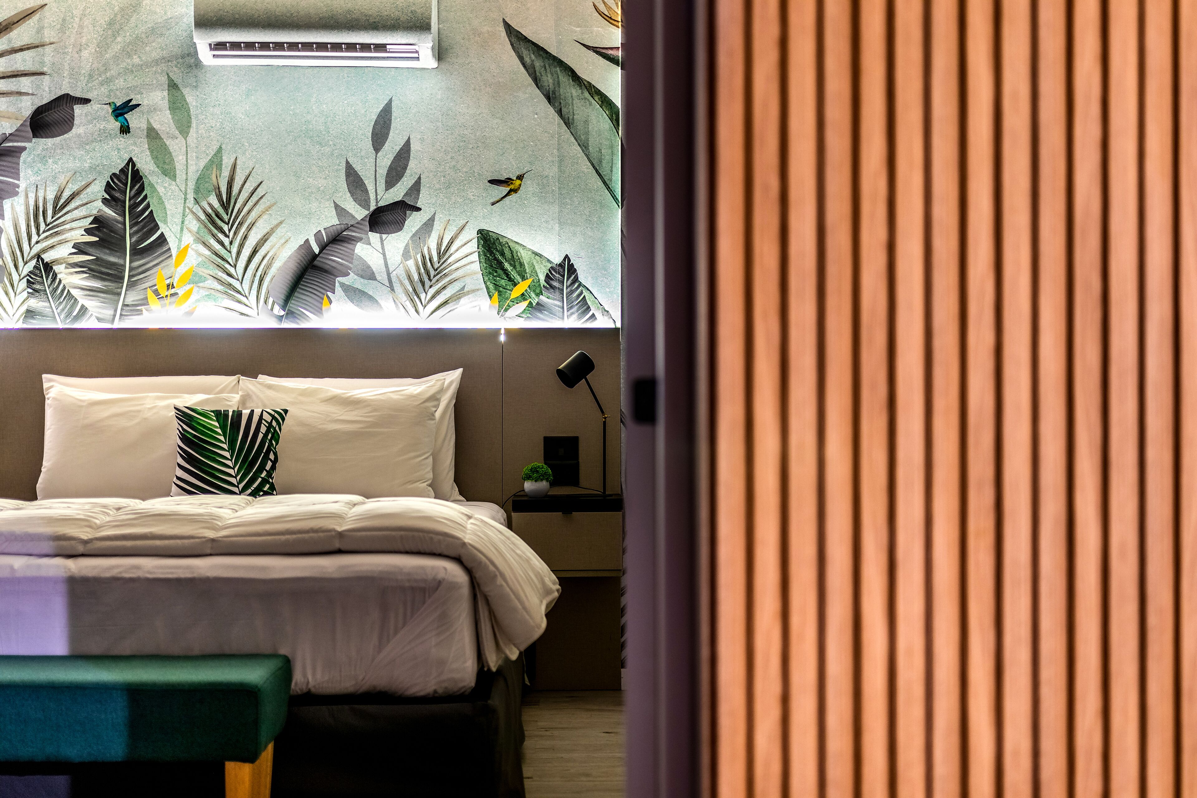 A bedroom with a bed, pillows, a bedside table, and a wall with a leaf pattern.