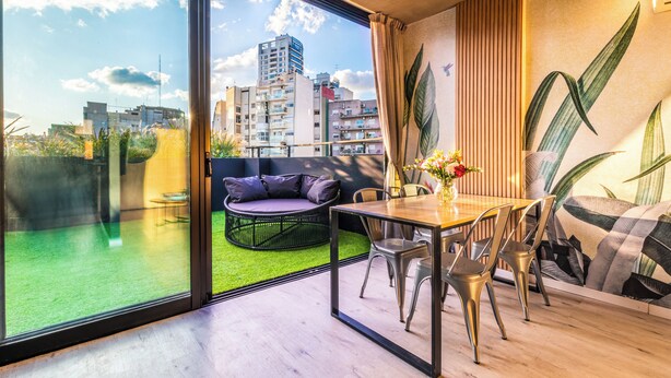 A modern living room with a glass wall, a dining table, and a sofa. - Deluxe Apartments in Palermo - by BueRentals (Buenos Aires)