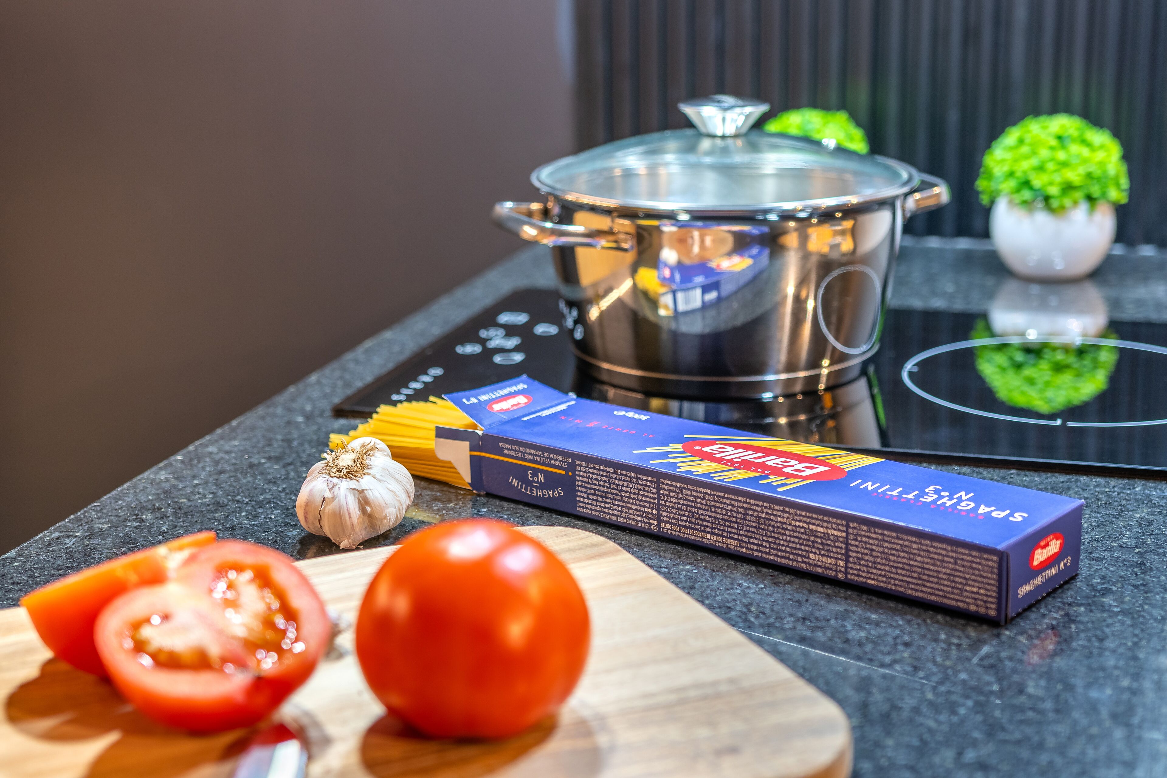 Una encimera de cocina con una olla, tomates, ajo y una caja de espagueti.