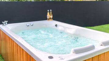 Un jacuzzi con dos botellas de cerveza, rodeado por una terraza de madera y un muro negro.