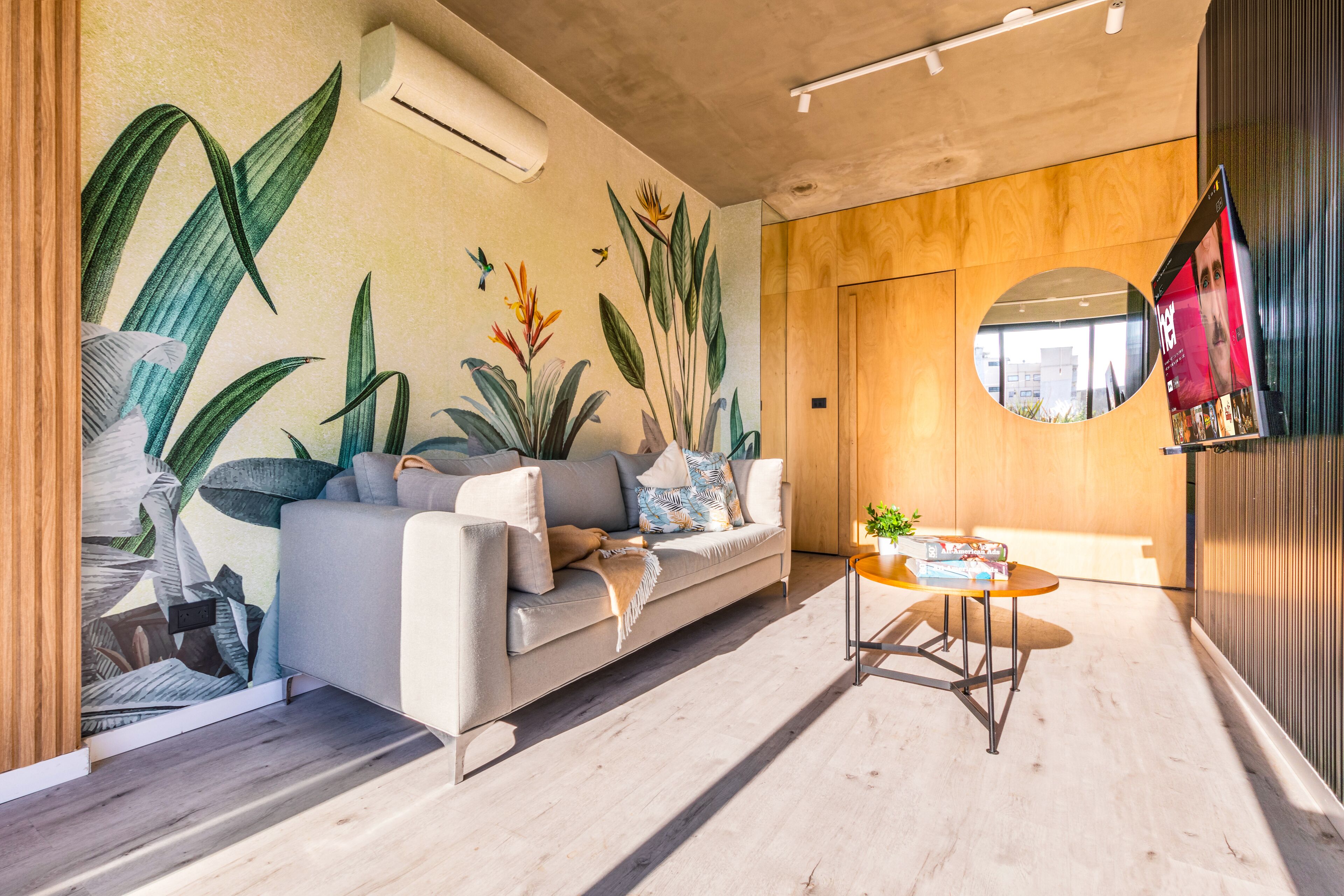 Un salon moderne avec un canapé, une table basse et une fresque représentant des plantes tropicales.