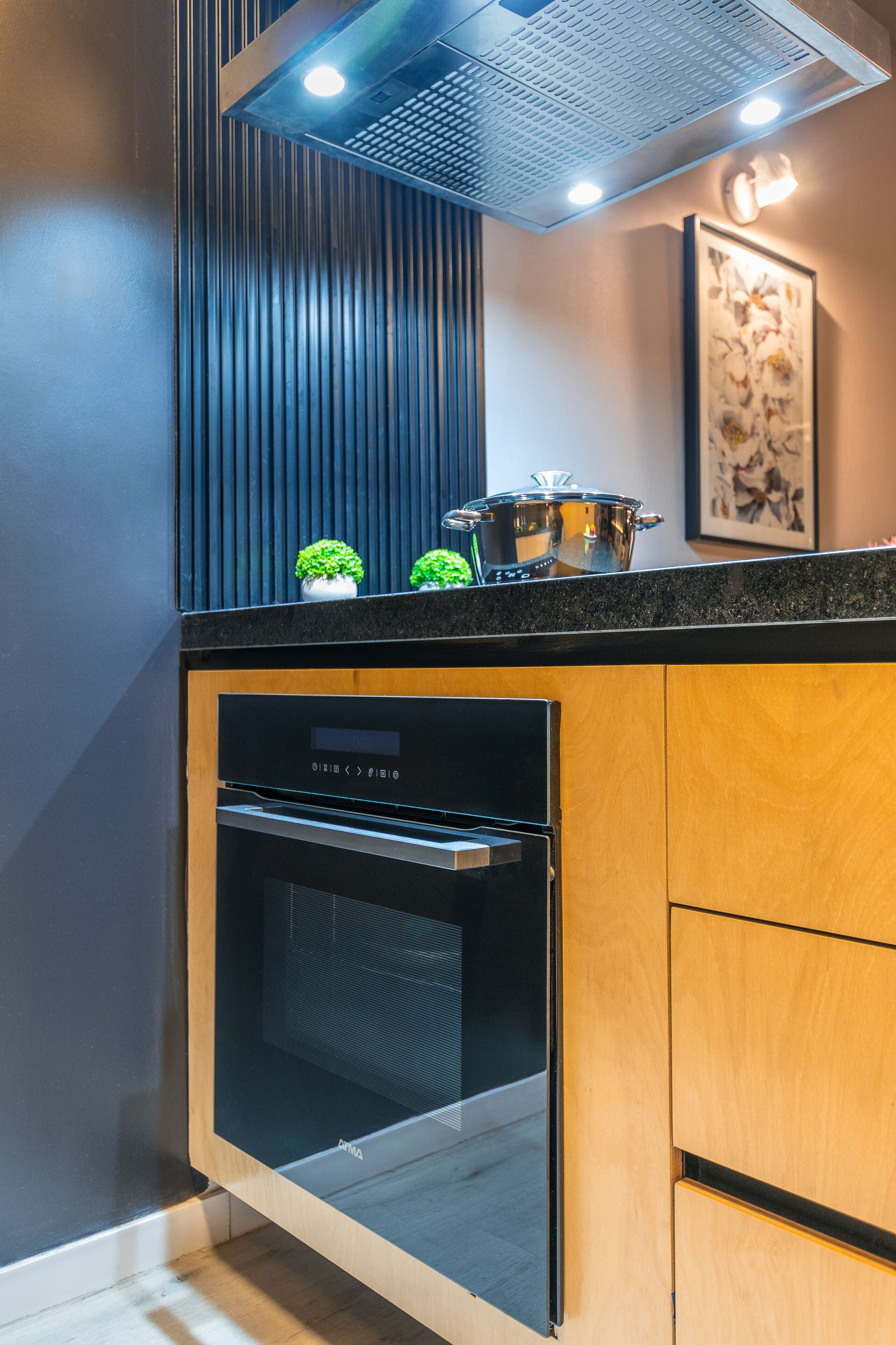 A modern kitchen with a built-in oven, a pot on the countertop, and a small potted plant.