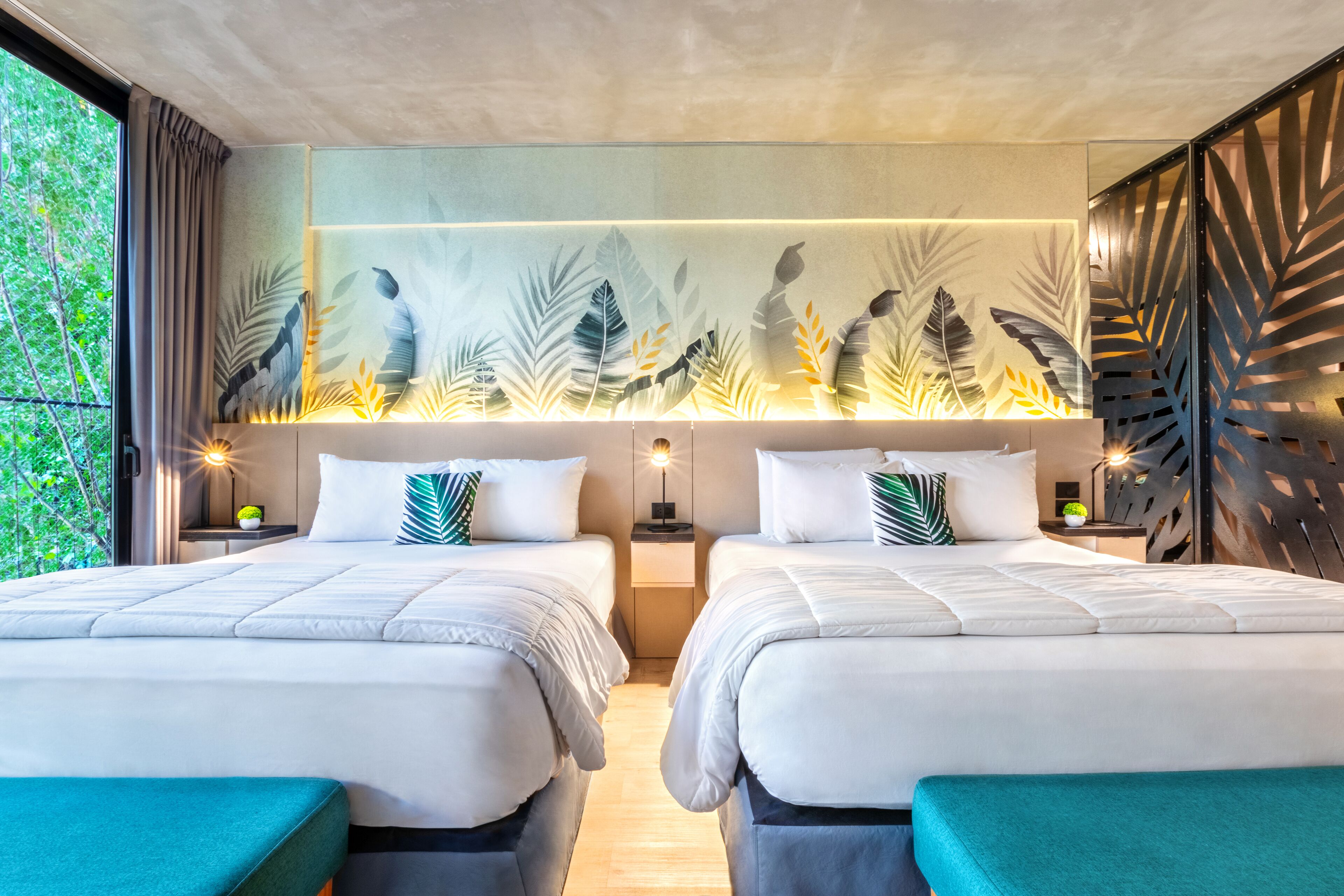 Ein modernes Hotelzimmer mit zwei Betten, einem großen Fenster und einer Wand mit einem Blattmuster.