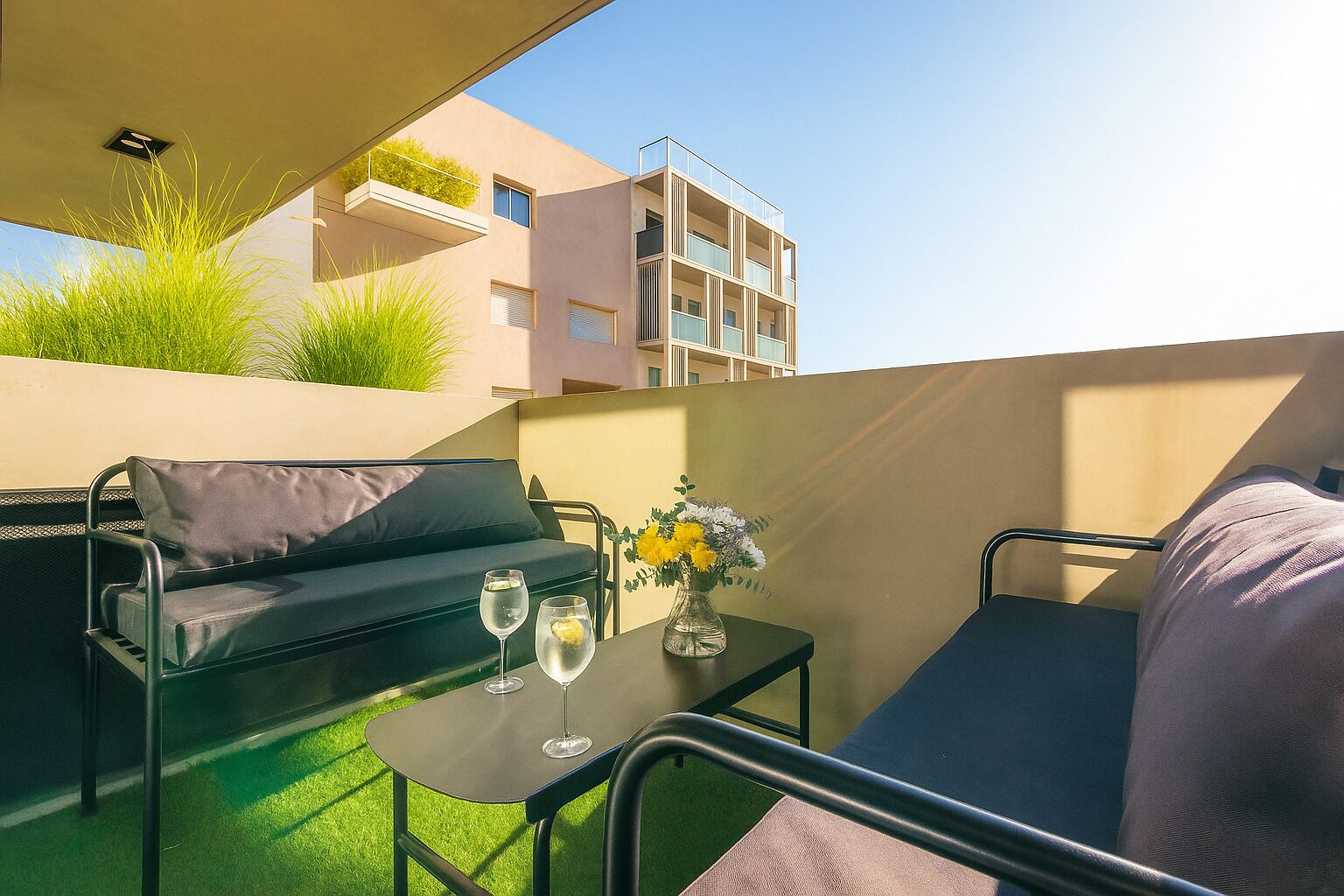 Ein Balkon mit einer Couch, einem kleinen Tisch und zwei Gläsern Wasser.