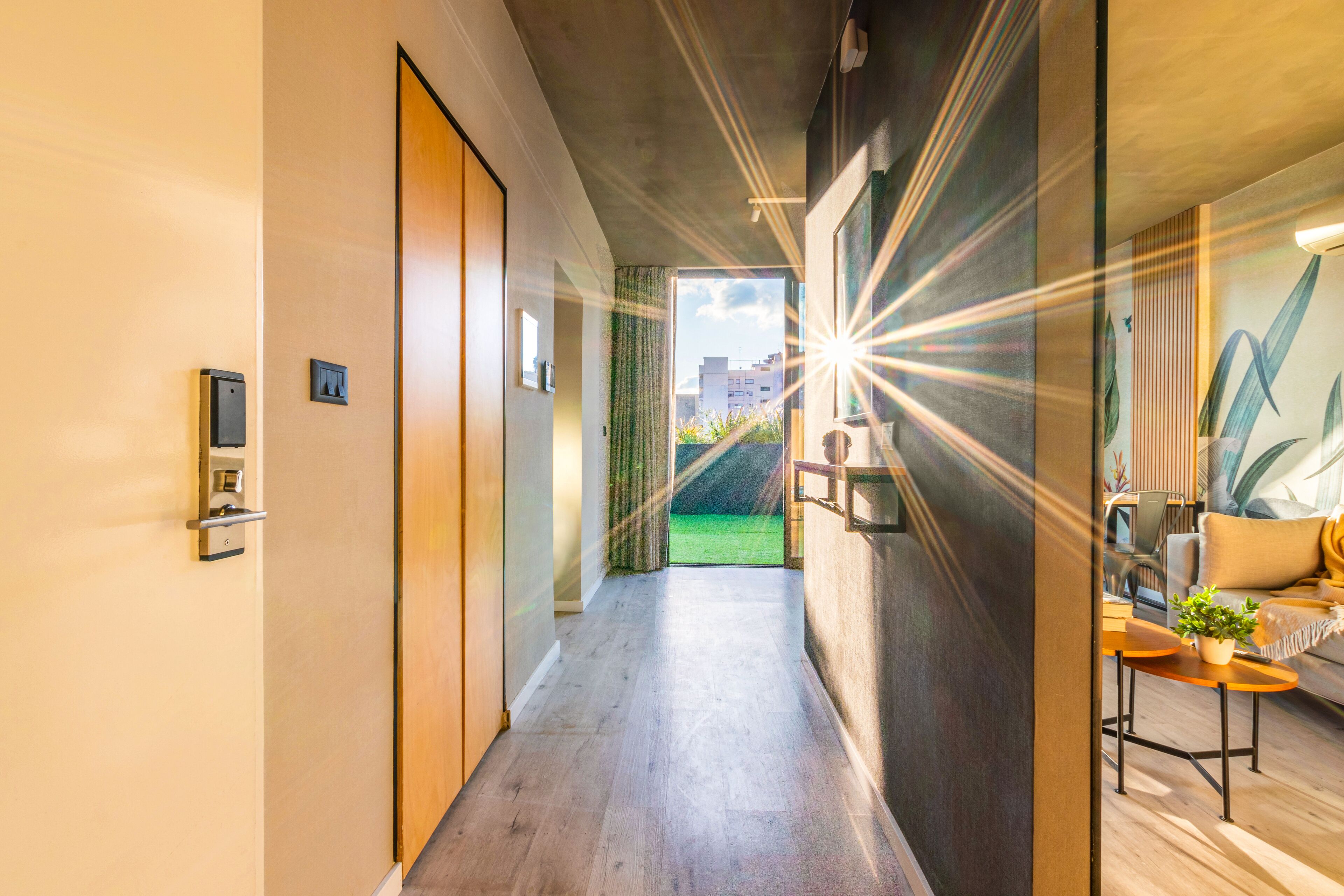 A modern hotel corridor with a wooden floor, a door with a keycard reader, and a view of the outdoors.