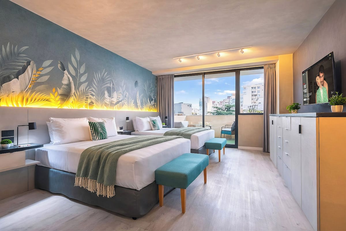 A modern hotel room with two beds, a large window, a mural, and a TV.