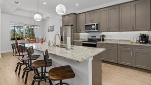 A modern kitchen with granite countertops, stainless steel appliances, and a central island with bar stools. - Villa Teal | Heated Pool & Spa Coral Oaks Golf Course (Cape Coral)