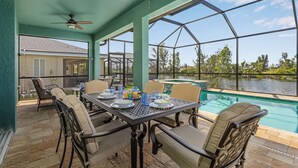 A patio area with a table set for dining, chairs, and a view of a swimming pool. - Villa Teal | Heated Pool & Spa Coral Oaks Golf Course (Cape Coral)