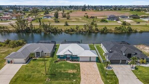 A residential area with houses near a lake, featuring a well-maintained lawn and a paved driveway. - Villa Teal | Heated Pool & Spa Coral Oaks Golf Course (Cape Coral)