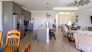 A modern kitchen with grey cabinets, a central island, and a dining area with chairs and a table. - Villa Teal | Heated Pool & Spa Coral Oaks Golf Course (Cape Coral)